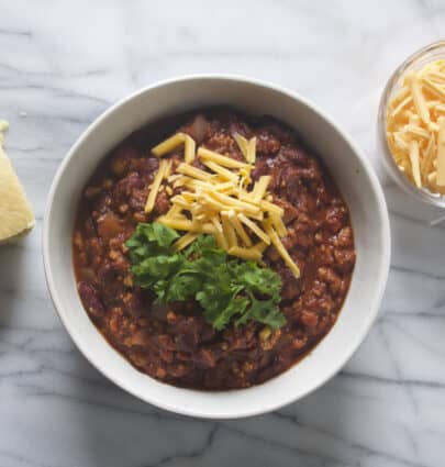 Vegan Tofu Chili in a bowl with a side of shredded vegan cheddar cheese and vegan cornbread