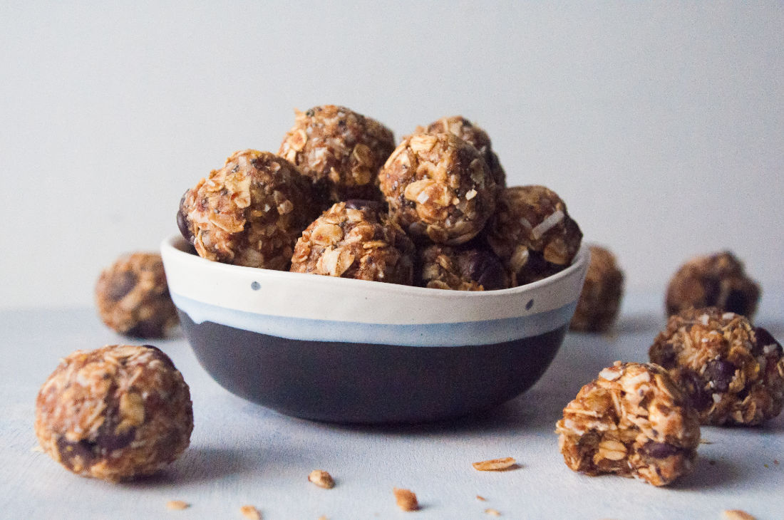 Energy bites piled in a bowl with more scattered around on the surface