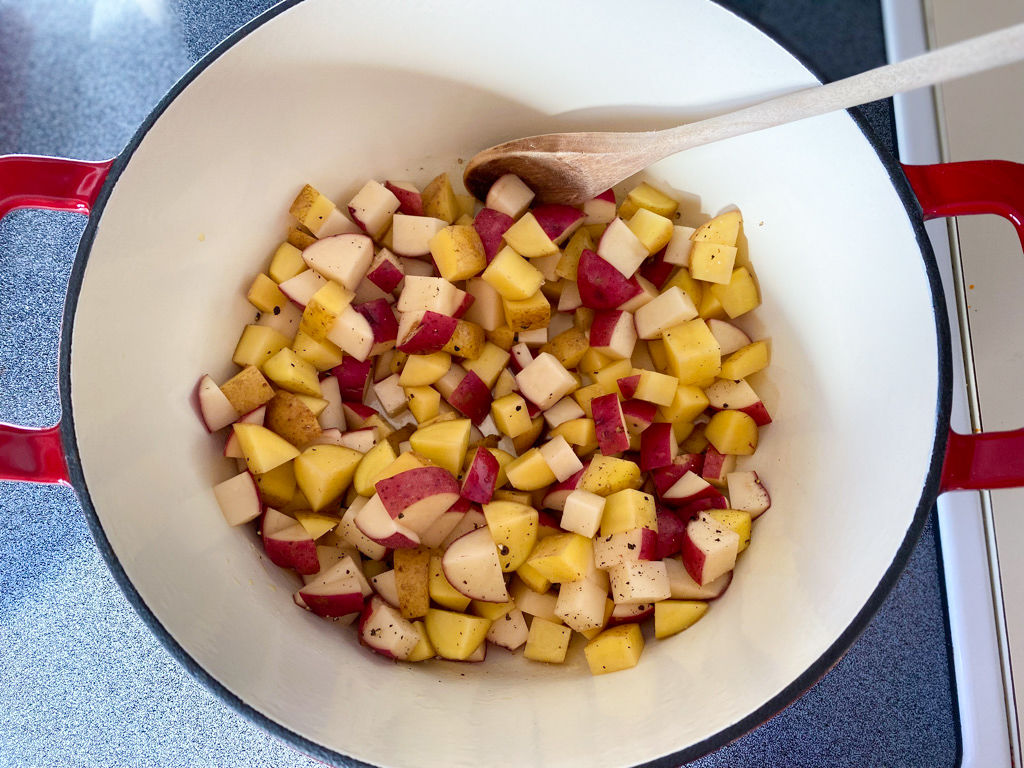 Red cast-iron pot on a stovetop filled with potatoes