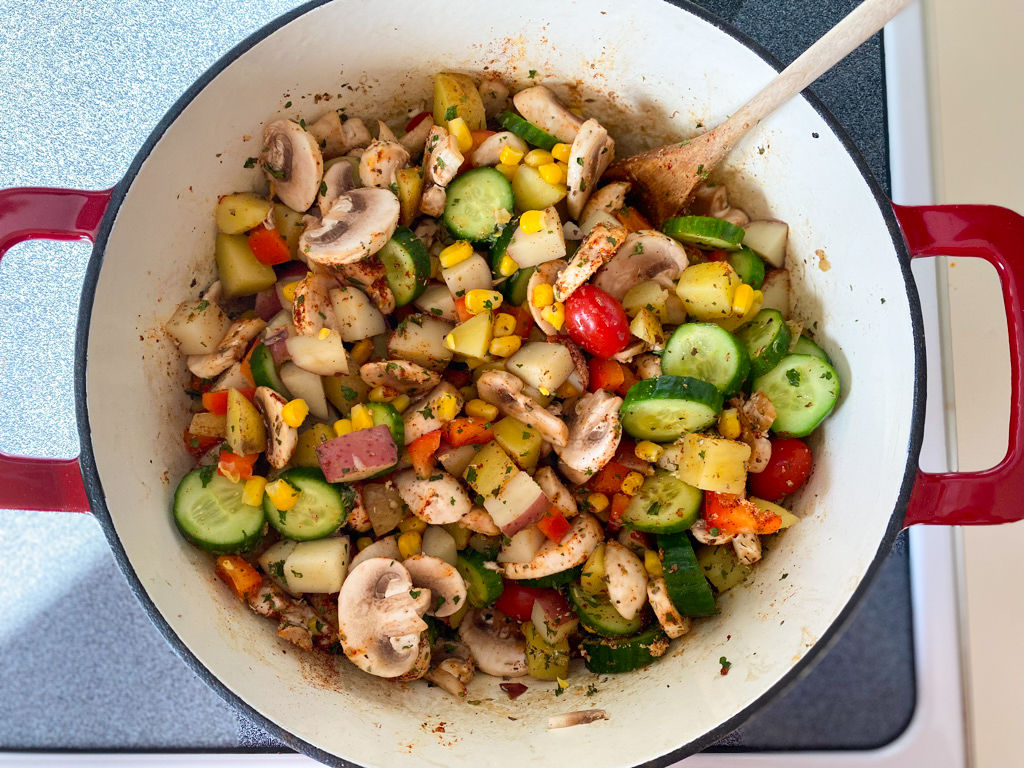 Red cast-iron pot on a stovetop filled with a vegetable hash